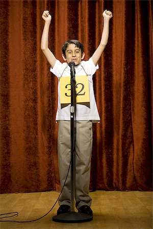 Boy contestant standing at microphone waving and smiling Stock Photo - Premium Royalty-Free, Code: 640-02774522