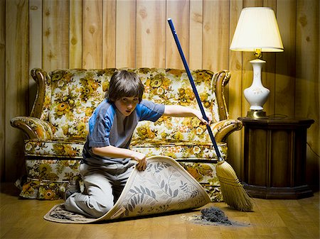 Boy sweeping dirt under rug Stock Photo - Premium Royalty-Free, Code: 640-02771083