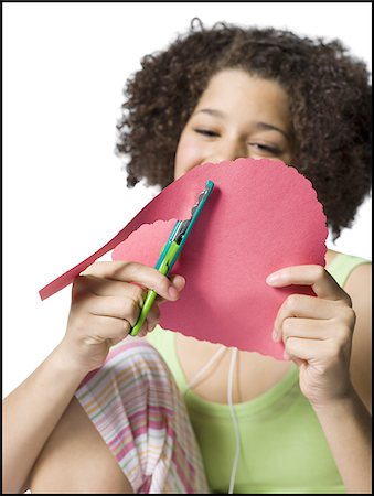 simsearch:640-02773530,k - Teenage girl with braces and ear buds cutting out hearts with scissors Stock Photo - Premium Royalty-Free, Code: 640-02772653