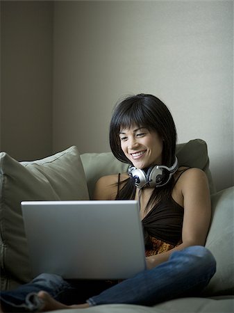 Woman sitting on sofa with laptop and headphones Stock Photo - Premium Royalty-Free, Code: 640-02772784