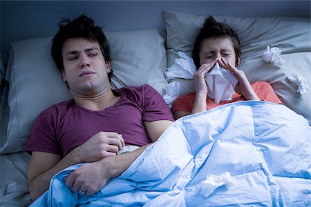 Man laying in bed with woman blowing nose with tissue Stock Photo - Premium Royalty-Free, Code: 640-02772852