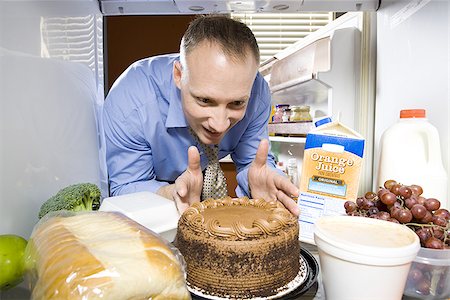 Man in refrigerator dipping finger in chocolate cake Stock Photo - Premium Royalty-Free, Code: 640-02773258