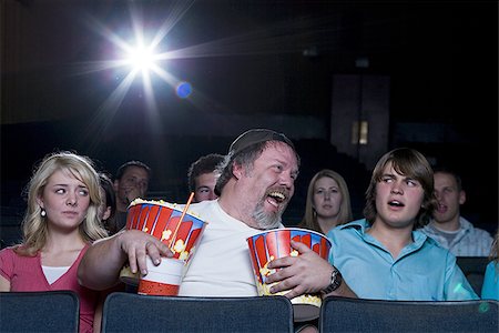 simsearch:640-02773406,k - Large man with buckets of popcorn and drink at movie theater between couple Stock Photo - Premium Royalty-Free, Code: 640-02773423