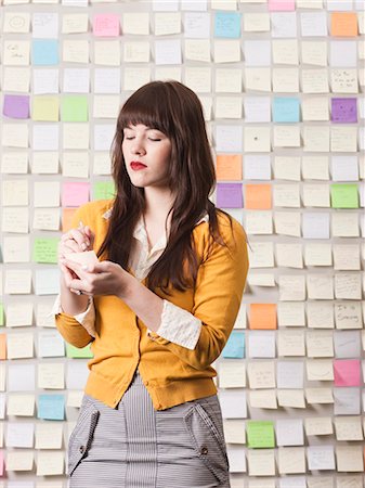 self adhesive note - Young woman writing in front of wall covered with adhesive notes Stock Photo - Premium Royalty-Free, Code: 640-03256368