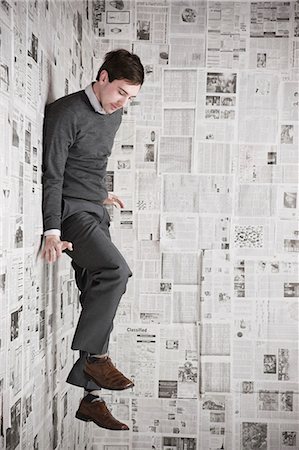 person surprised and scared full body - Young man stuck to wall covered with newspapers, studio shot Stock Photo - Premium Royalty-Free, Code: 640-03256378