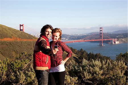 USA, California, San Francisco, young couple photographing themselves with Golden Gate Bridge in background, portrait Stock Photo - Premium Royalty-Free, Code: 640-03257283