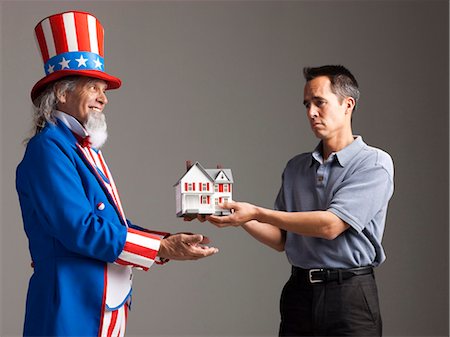 Man in Uncle Sam's costume giving model of house to other man, studio shot Stock Photo - Premium Royalty-Free, Code: 640-03257659