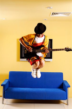 picture of the blue playing a instruments - Fashionable young man jumping and playing guitar in front of blue sofa Stock Photo - Premium Royalty-Free, Code: 642-01736867