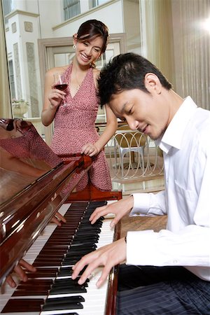 Young man playing piano while woman listening and holding wine glass Stock Photo - Premium Royalty-Free, Code: 642-01737553