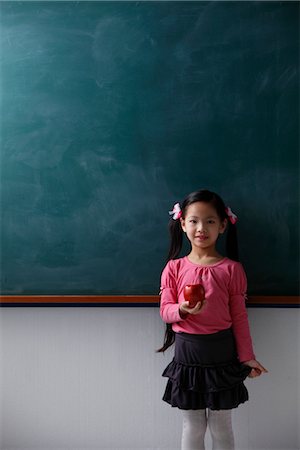 Young girl holding red apple in front of chalk board Stock Photo - Premium Royalty-Free, Code: 656-04926472