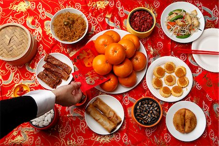 Hand reaching for red envelope (Hong Bao) on table set for Chinese New Year. Stock Photo - Premium Royalty-Free, Code: 656-04926497