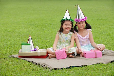 Two girls wearing party hats sitting on picnic blanket, surrounded by gifts Stock Photo - Premium Royalty-Free, Code: 656-01765361