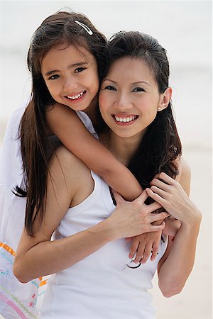 Daughter behind mother with arms over shoulders, smiling, hugging, on the beach Stock Photo - Premium Royalty-Free, Code: 656-01765384