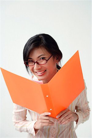 spur - A woman smiles at the camera as she holds an orange folder Stock Photo - Premium Royalty-Free, Code: 656-01766403