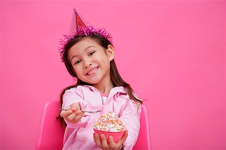 Girl wearing party hat, holding bowl of cake towards camera Stock Photo - Premium Royalty-Free, Code: 656-01772804