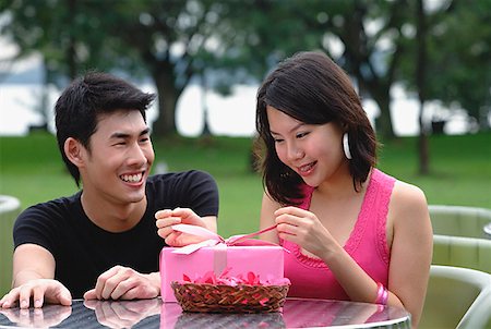 Woman unwrapping a gift, man crouching next to her, smiling Stock Photo - Premium Royalty-Free, Code: 656-01773938