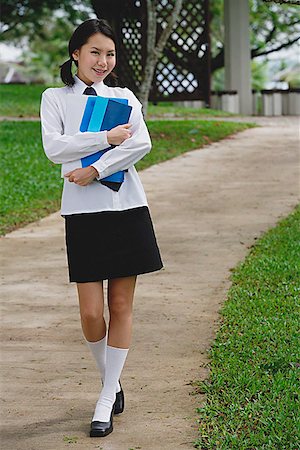 Young woman in school uniform, walking on path, smiling at camera Stock Photo - Premium Royalty-Free, Code: 656-01773946