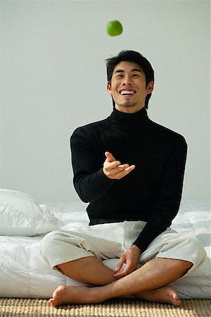 Young man sitting on bed, throwing apple in the air Stock Photo - Premium Royalty-Free, Code: 656-01828857