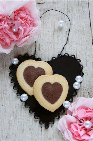 Bi-coloured heart-shaped biscuits on a black metal heart between paper carnations Stock Photo - Premium Royalty-Free, Code: 659-06373505