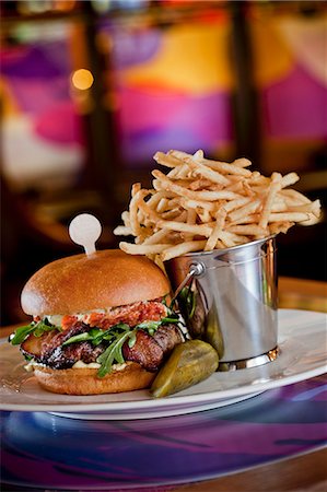 Beef Sirloin Burger with Smoked Bacon, Aged Goat Cheddar Cheese, Tomato Confit, Baby Arugula and Garlic Chive Aioli; Pickle and French Fries Stock Photo - Premium Royalty-Free, Code: 659-06670885