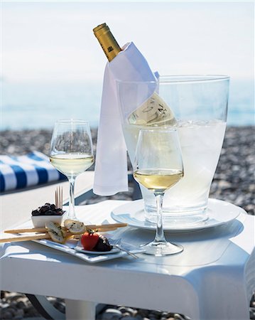 A table laid for two at the beach, with appetisers, glasses of white wine and a bottle of wine in a chiller Stock Photo - Premium Royalty-Free, Code: 659-06671229