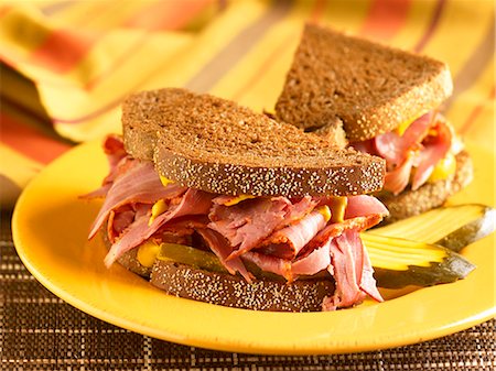 Corned Beef Sandwich with Mustard and Pickles on Pumpernickel Bread; Halved on a Yellow Plate Photographie de stock - Premium Libres de Droits, Code: 659-06901387