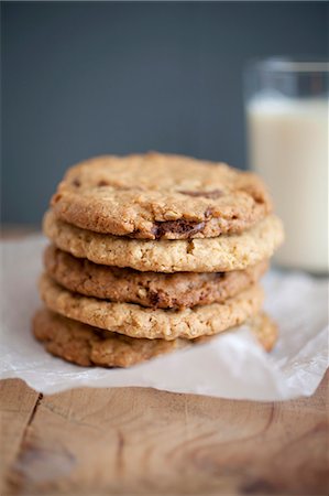 frosted - Chocolate chip, peanut butter and oatmeal cookies stacked on baking parchment wih a glass of milk in the background. Stock Photo - Premium Royalty-Free, Code: 659-06903530