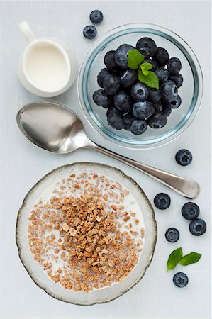 A bowl of crunchy breakfast cereal drenched in milk and a bowl of fresh blueberries Stock Photo - Premium Royalty-Free, Code: 659-07739472