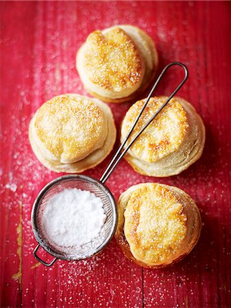 Mince pies and a sieve of icing sugar on a red wooden surface Stock Photo - Premium Royalty-Free, Code: 659-07958772