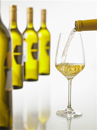 simsearch:659-06186663,k - White white being poured into a glass with a row of wine bottles in the background Stock Photo - Premium Royalty-Free, Code: 659-08420081