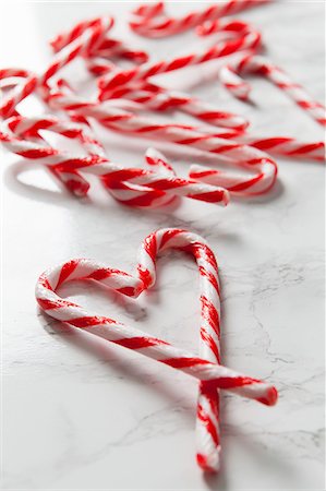 simsearch:659-07069631,k - White marble surface covered in candy canes and two canes in the foreground forming a heart shape Stock Photo - Premium Royalty-Free, Code: 659-08896351