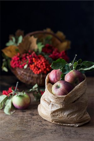 Apples in a paper bag in front of a basket of rowan berries Foto de stock - Sin royalties Premium, Código: 659-08896413