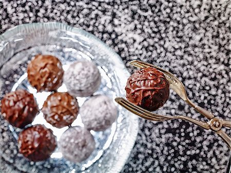 simsearch:841-06805239,k - Praline tongs holding a truffle praline over a glass plate of various truffles Stock Photo - Premium Royalty-Free, Code: 659-08904648