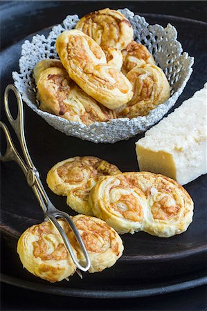 Savoury puff pastries with Parmesan cheese on a black plate with a pair of pastry tongs Stock Photo - Premium Royalty-Free, Code: 659-08904739