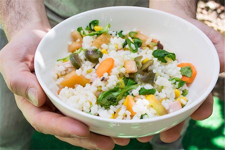 Hands holding a bowl of rice salad with tomatoes, basil, olive oil, olives, sweetcorn and carrots Stock Photo - Premium Royalty-Free, Code: 659-08905746