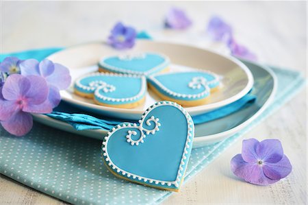 simsearch:659-06903190,k - Heart-shaped biscuits decorated with blue and white icing served on a plate with flowers Stock Photo - Premium Royalty-Free, Code: 659-08905974