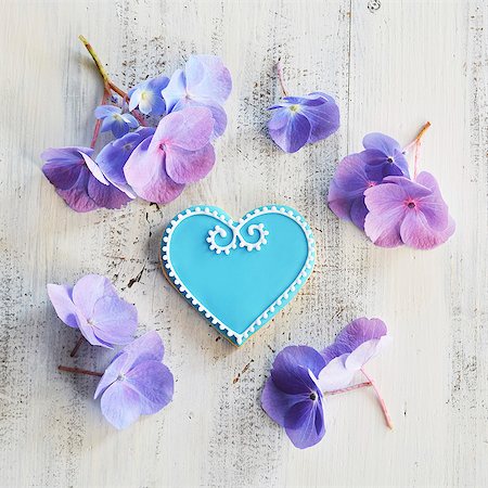 Heart-shaped biscuits decorated with blue and white icing and surrounded by flowers Stock Photo - Premium Royalty-Free, Code: 659-08905975