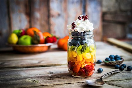 A colourful fruit salad in a jar topped with cream and pomegranate seeds on a rustic wooden surface Stock Photo - Premium Royalty-Free, Code: 659-08940004