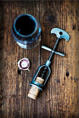 An antique corkscrew with a cork, and a glass of red wine on a wooden surface Stock Photo - Premium Royalty-Free, Code: 659-09125405