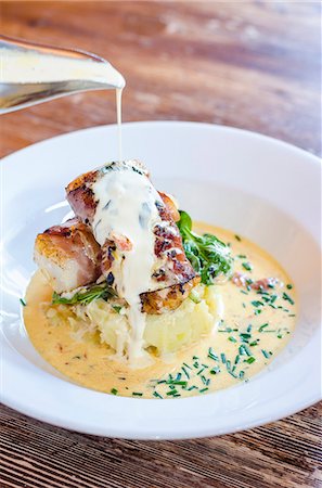 simsearch:659-06372915,k - Sea bass fish fillets wrapped in bacon on a potato mash with spinach and chives with a pour of white wine sauce Stock Photo - Premium Royalty-Free, Code: 659-09125893