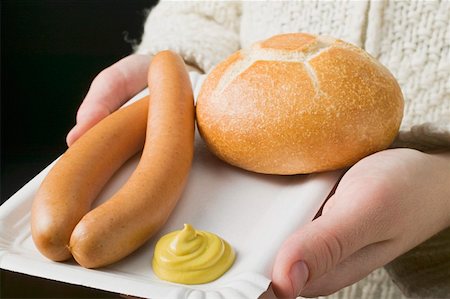 Person holding frankfurters, roll & mustard on paper plate Stock Photo - Premium Royalty-Free, Code: 659-01862281