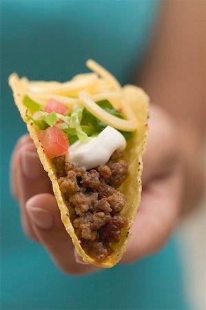 Hand holding taco filled with mince, cheese & sour cream Stock Photo - Premium Royalty-Free, Code: 659-02212515