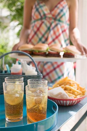 Iced tea and chips on table, woman serving hamburgers Stock Photo - Premium Royalty-Free, Code: 659-02212668