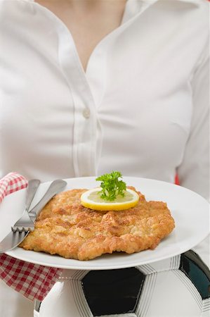 simsearch:659-02213122,k - Woman holding plate of Wiener schnitzel (veal escalope) on football Stock Photo - Premium Royalty-Free, Code: 659-02213125