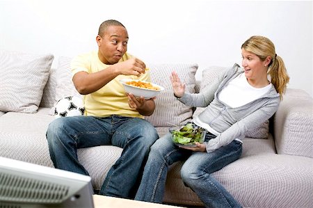 Couple with peanut puffs and salad in front of TV Stock Photo - Premium Royalty-Free, Code: 659-02213859