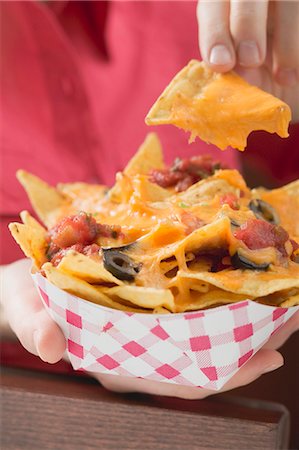 Woman holding nachos with melted cheese in cardboard container Stock Photo - Premium Royalty-Free, Code: 659-03527127