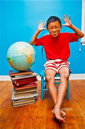 Boy making face next to books and globe Stock Photo - Premium Royalty-Free, Code: 673-06025416