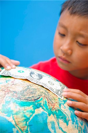 Boy placing dollar bill on globe Stock Photo - Premium Royalty-Free, Code: 673-06025499