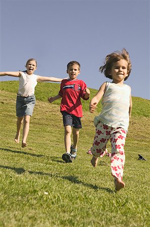 Three young siblings running down a grassy hill. Stock Photo - Premium Royalty-Free, Code: 673-02137915