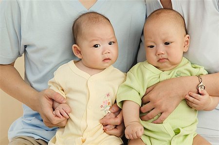 Twins sitting side by side on their parents' laps. Stock Photo - Premium Royalty-Free, Code: 673-02138327